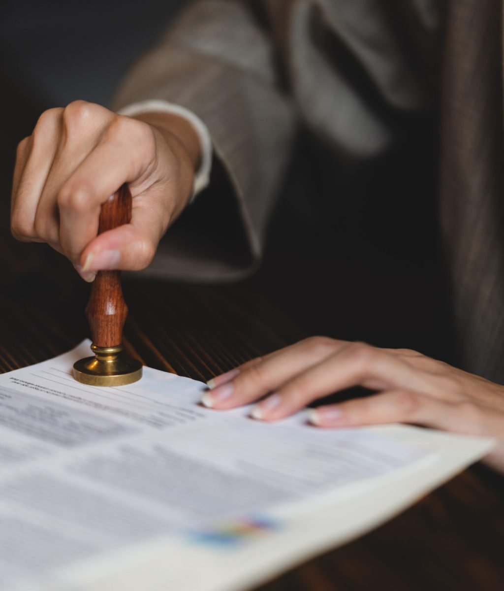 Close-up of a person's hand stamping with approved stamp on certificate document public paper at desk, notary or business people work from home, isolated for coronavirus COVID-19 protection